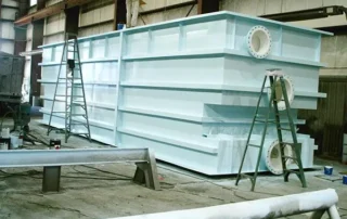 Stiffened flat-sided industrial storage tank with external structural ribs under fabrication inside an engineering workshop